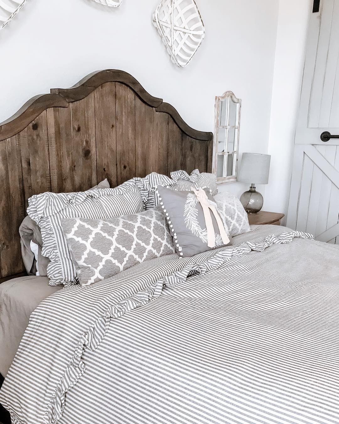 A rustic bedroom featuring a wooden headboard, modern farmhouse bedding, and decorative pillows, with a neutral color palette.