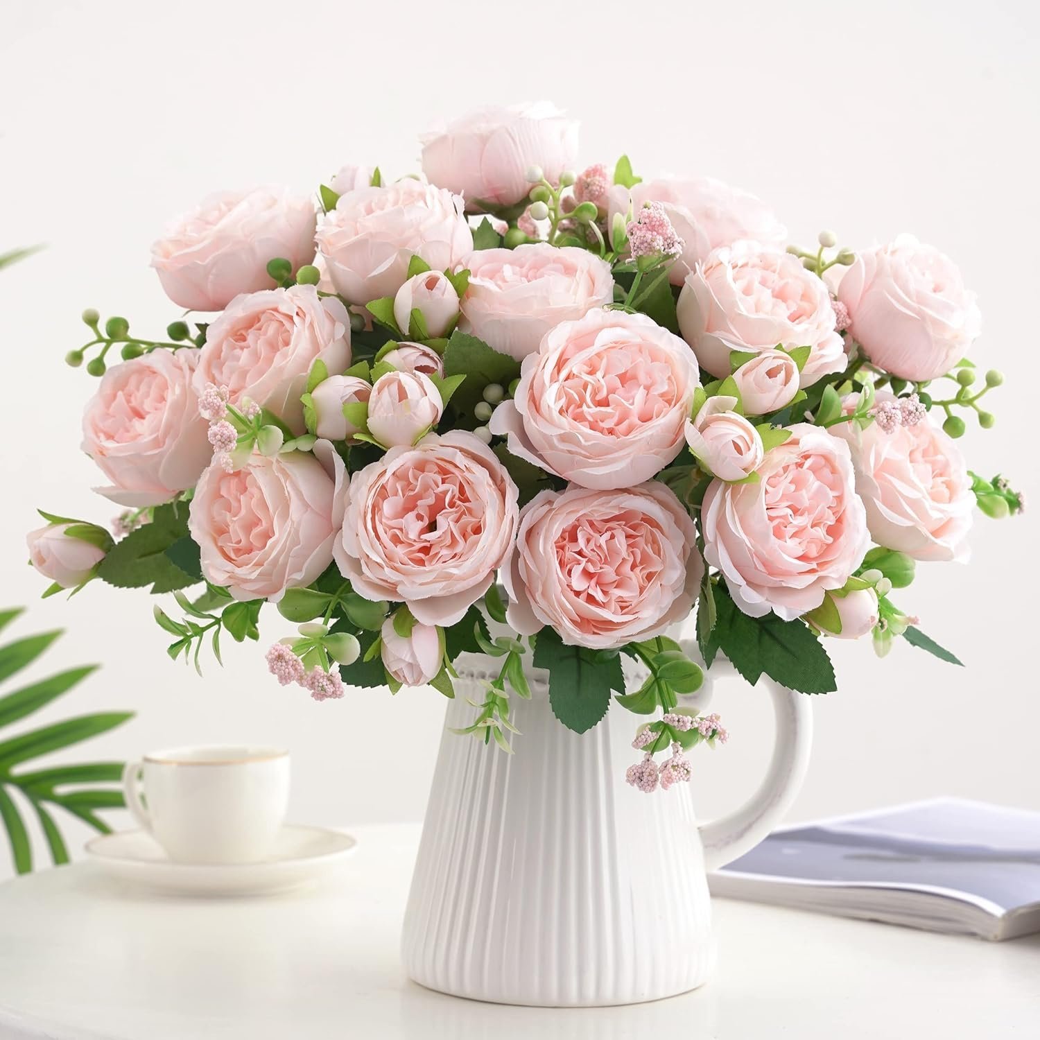 artificial pink silk peony styled in a white ceramic vase on a table