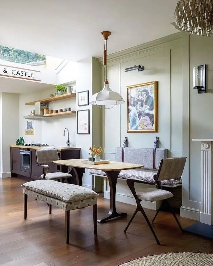 A stylish kitchen and dining area with a wooden table, modern banquette seating, and elegant decor. A large painting hangs on the wall, with pendant lights and built-in cabinets.