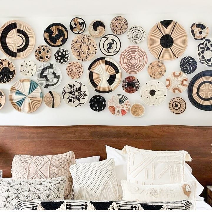Decorative wall with various Bohemian patterned round baskets above a bed adorned with textured pillows and blankets.