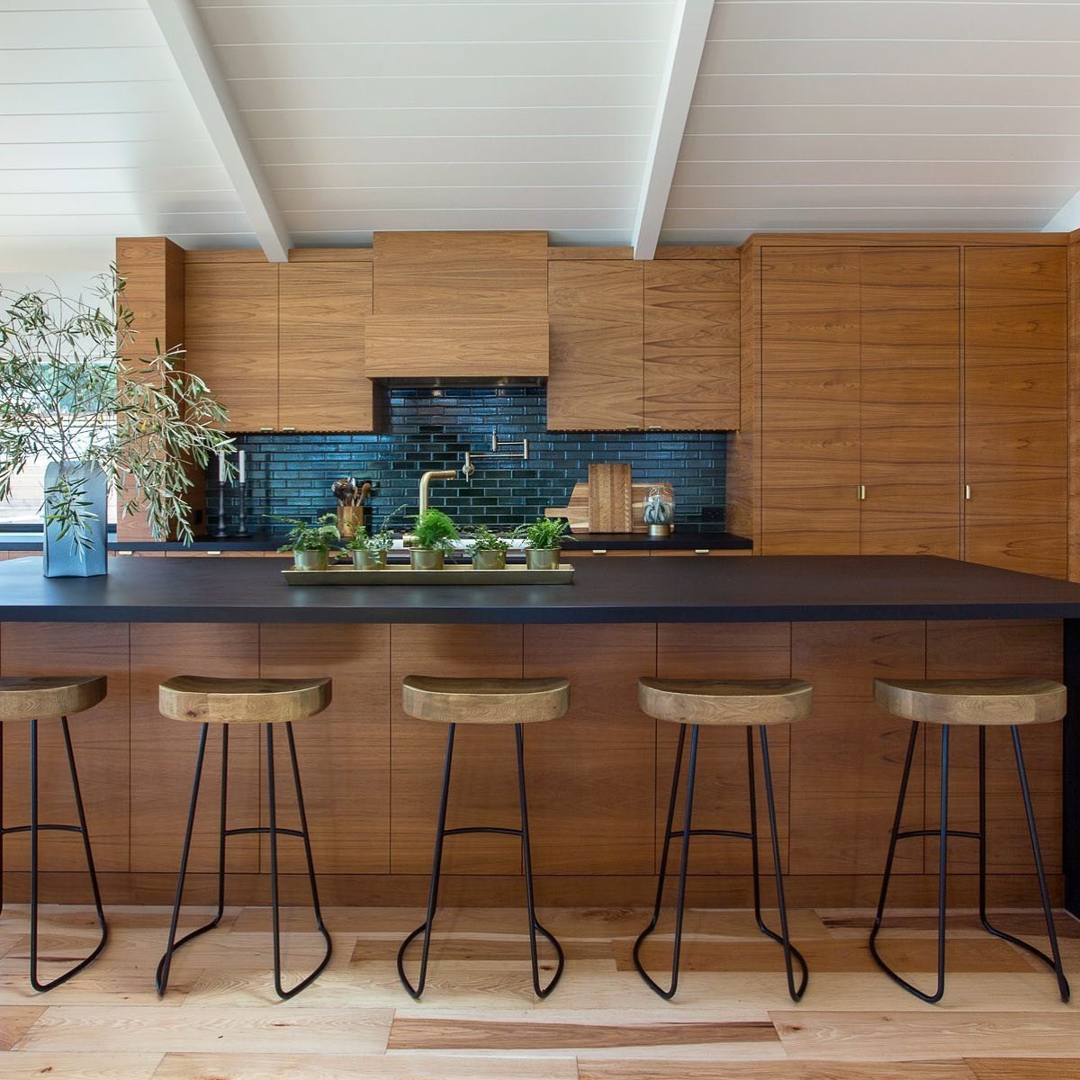 Modern kitchen with wooden cabinets, black countertop, bar stools, and a dark blue tile backsplash featuring Top 10 Timeless Mid-Century Kitchen Design Features.