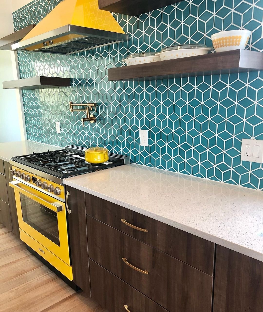 A modern kitchen featuring teal hexagonal tile backsplash, a yellow stove inspired by top 10 timeless Mid-Century design features, and dark wood cabinets under white countertops.