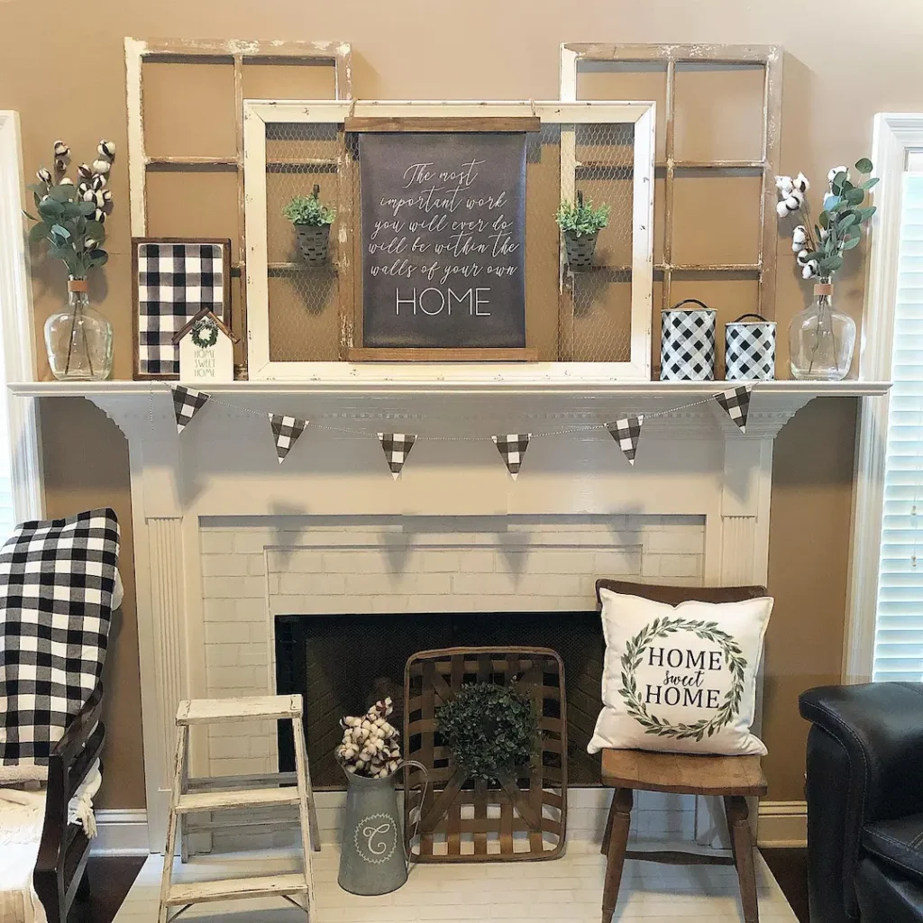 A white fireplace mantel is decorated with vases, greenery, framed signs, and checkered accents. A wooden chair and small ladder sit in front, showing how to embrace buffalo plaid in fall decor with pillows and other farmhouse details.