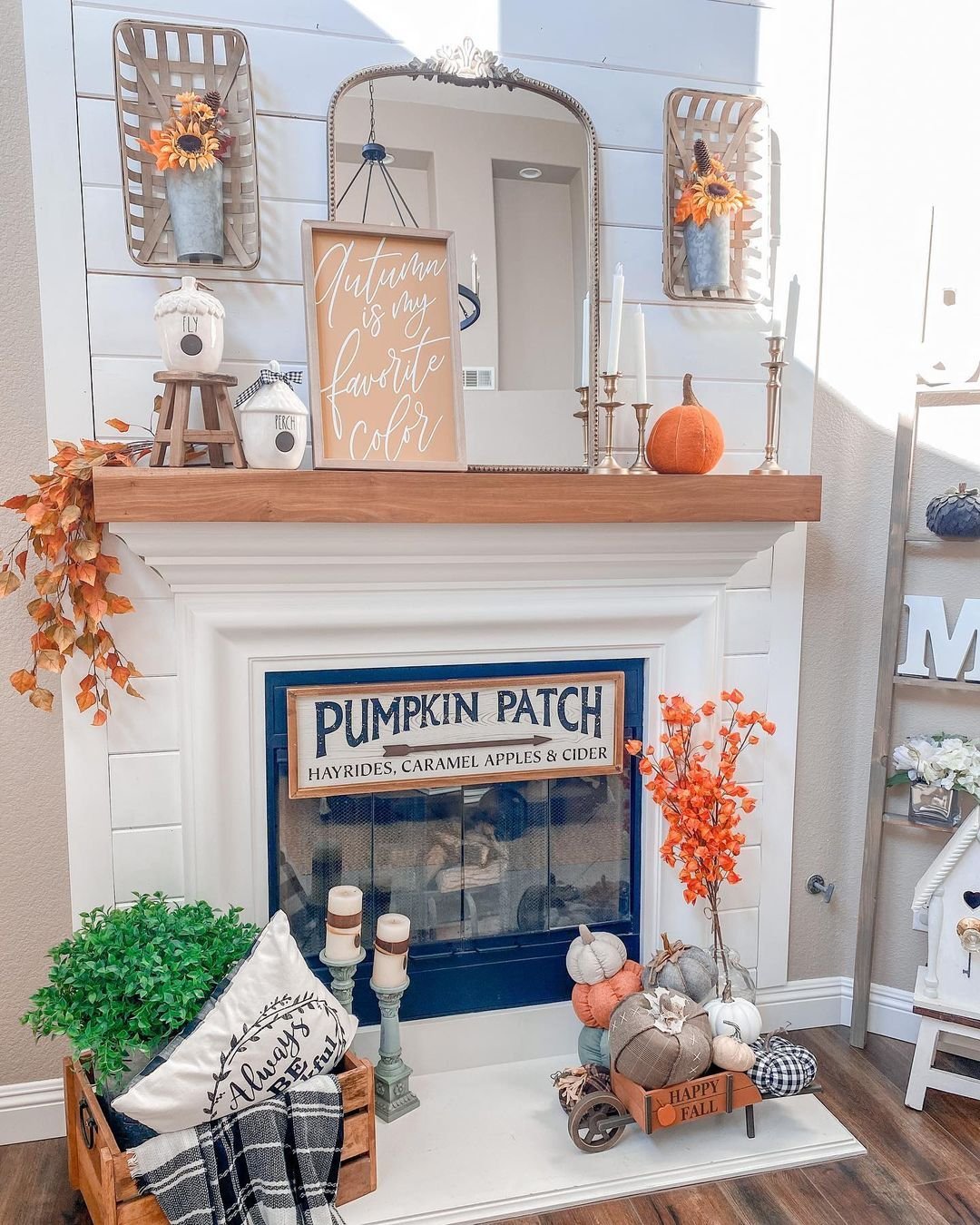 A white fireplace decorated with autumn-themed items such as pumpkins, candles, a fall sign saying "Autumn is my favorite color," leafy garlands, and a wooden tray with phrases on a blue and white background offers neutral fall mantel decor ideas for a chic and sophisticated look.