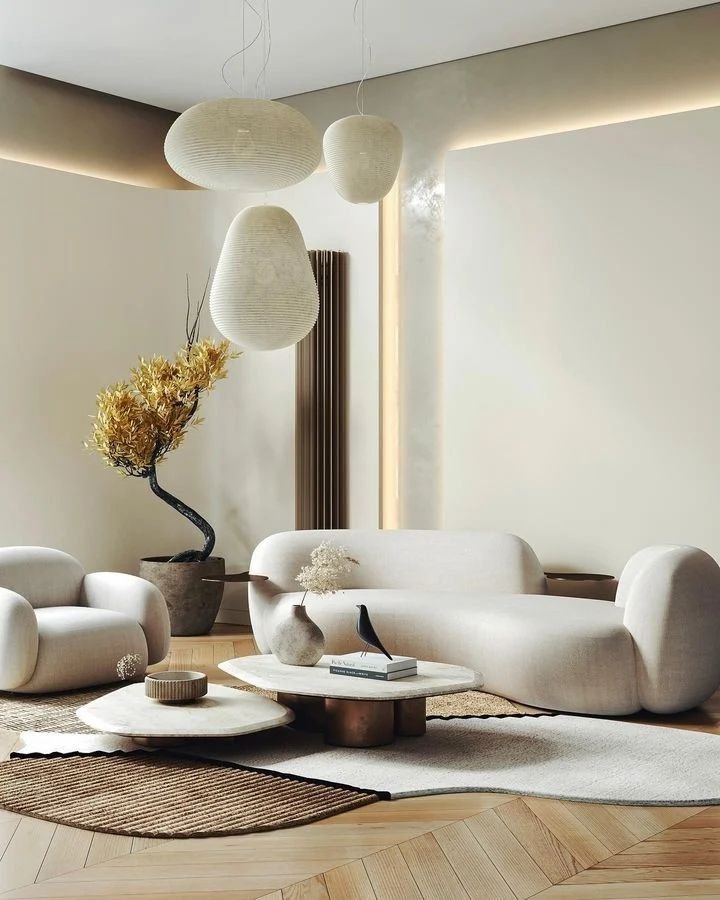 Minimalist living room with modern beige furniture, abstract pendant lights, a bonsai tree, and tiered coffee tables on a rug—an embodiment of Minimalist Living: How Japandi Decor Can Help Simplify Your Life.
