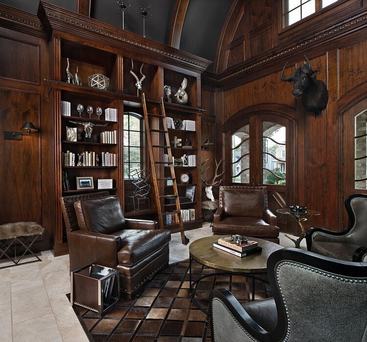 Wood-paneled room with high shelves, a ladder, leather seating, a round coffee table, and taxidermy on the walls. An inviting space that could easily feature in "10 Inspiring Home Office Library Designs for Every Decor Style.