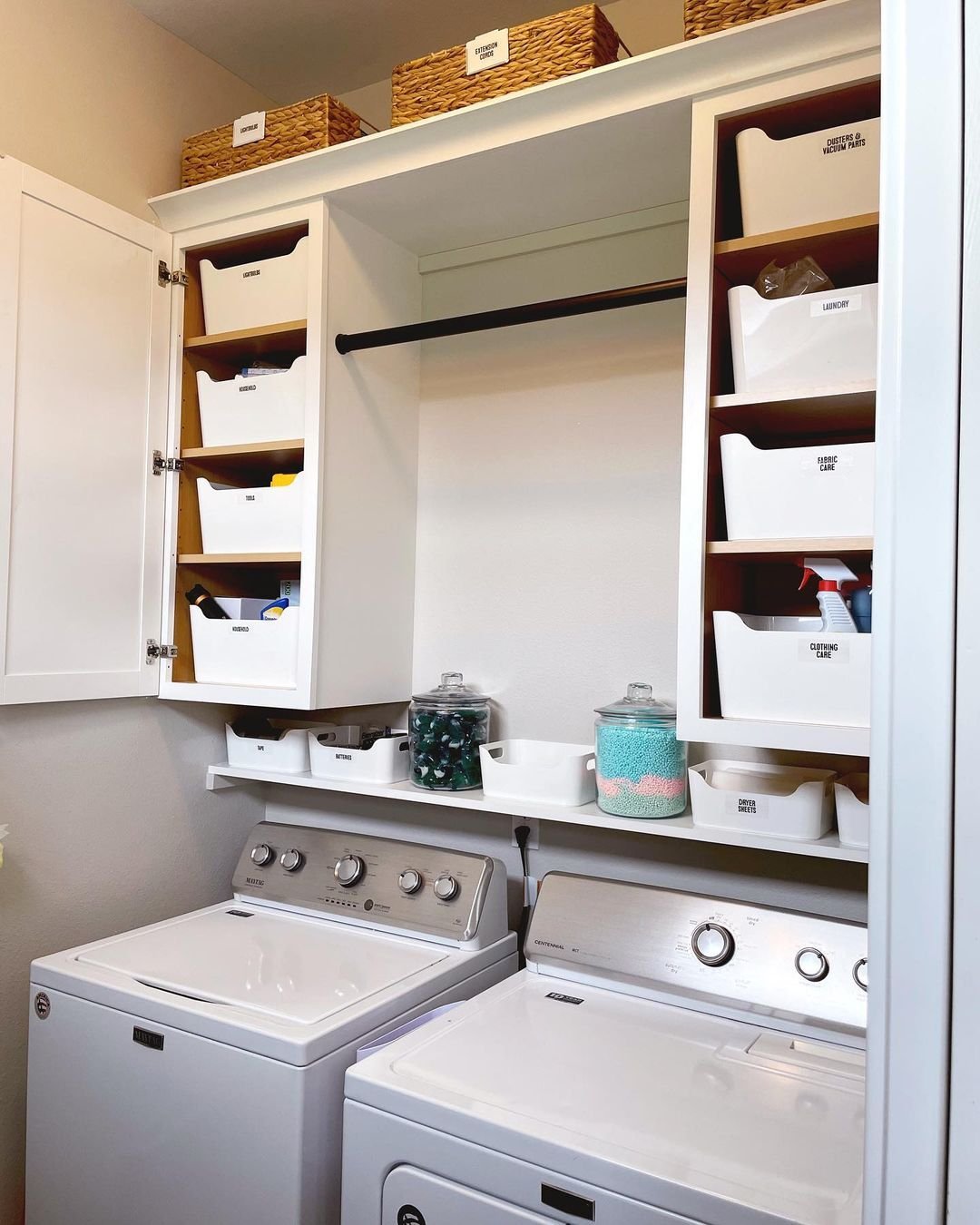 A well-organized laundry room with a washing machine and dryer below cabinets containing labeled storage bins and jars filled with laundry supplies highlights how creative storage hacks can transform your laundry area.
