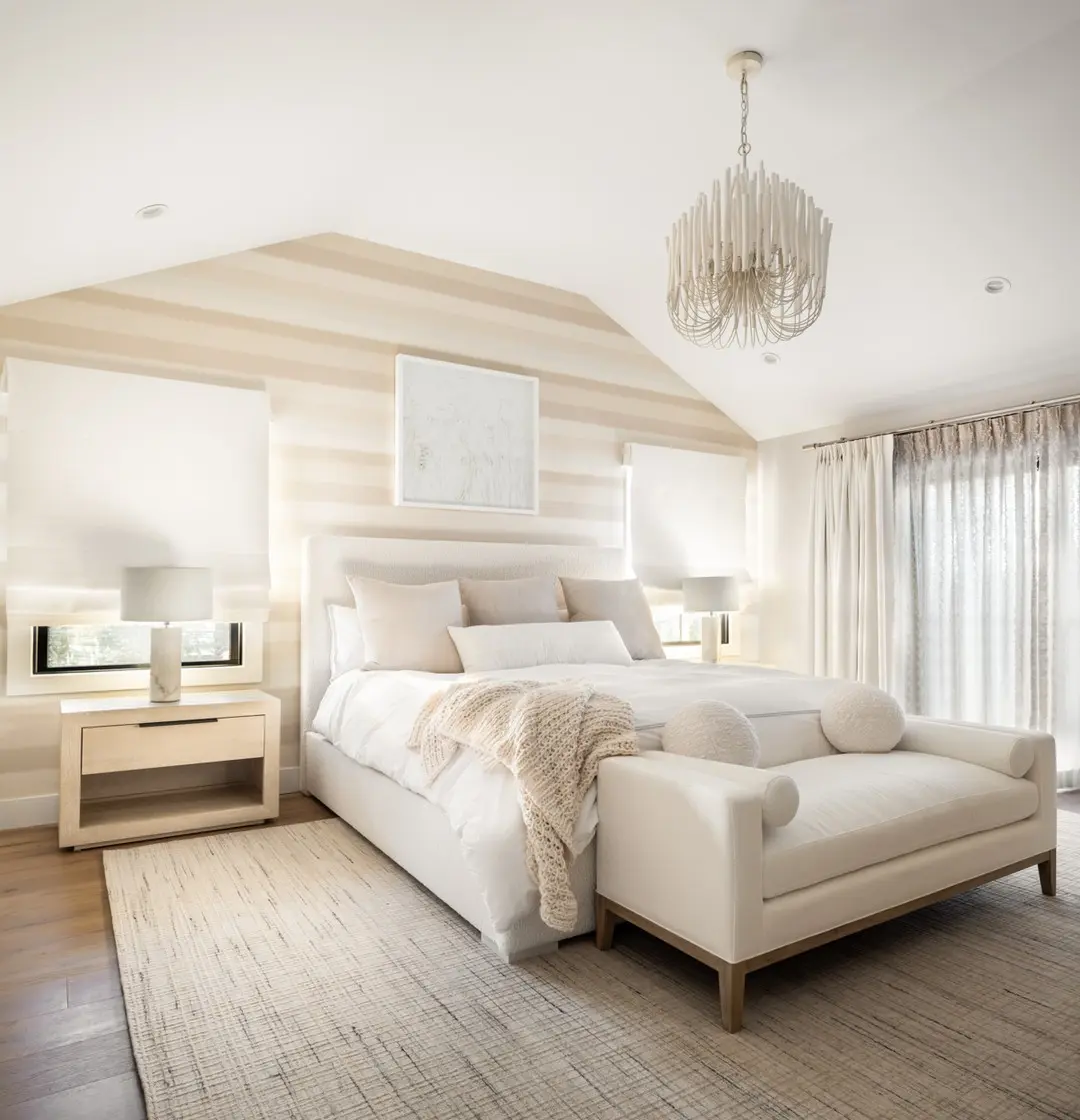 A modern bedroom with a large bed, two bedside tables with lamps, and neutral-toned decor illustrates how minimalism influences the creation of a sense of space, enhanced by sunlight filtering through sheer curtains.