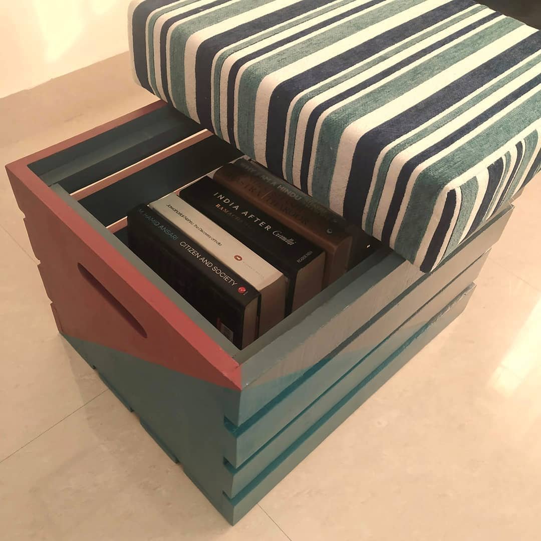 A wooden storage ottoman with a striped cushioned seat is open, revealing several books stored inside. For more inspiration, explore our list of "10 Wooden Crates Decor Hacks to Add Rustic Charm to Your Home.