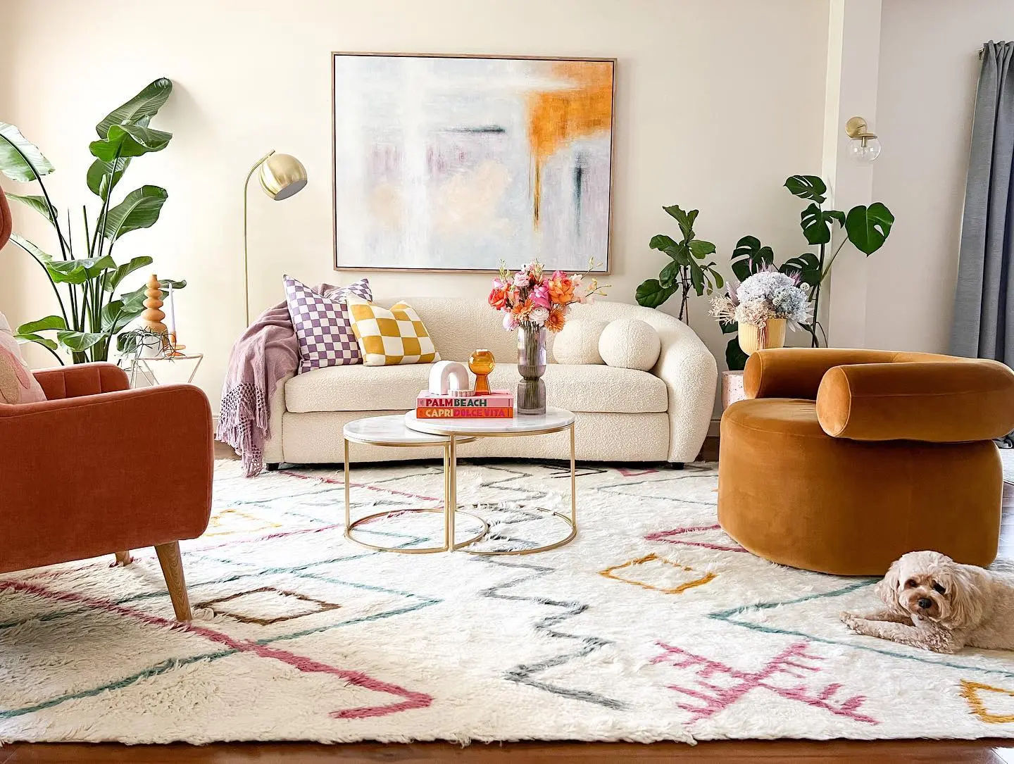 A modern living room with funky furniture, including a white sofa, orange chairs, round coffee table, abstract wall art, geometric rug, potted plants, and a small dog lying on the floor—unique pieces to make your home stand out.