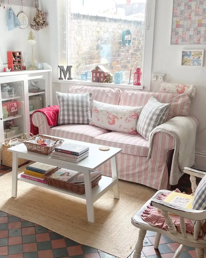 A cozy living room with a pink-striped sofa, patterned pillows, a white coffee table with books and baskets, and a woven rug adds charm to the checkered tile flooring—perfect for fans of buffalo check decor.